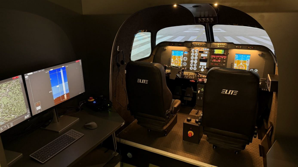 Official ELITE photograph showing a multi-crew flight simulator cockpit with projected runway imagery.
